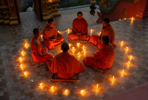 Close up group of young and senior monk sit in a circle with several lighting candle around in area of front of chapel or church for meditation in early morning.