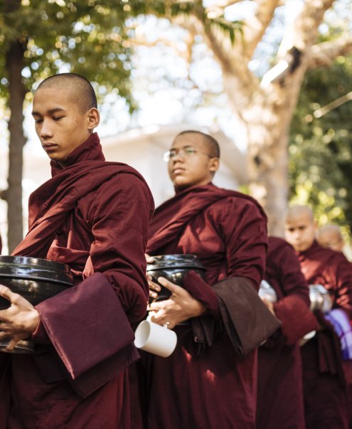 Monks in maroon robes lining up for alms in serene morning light